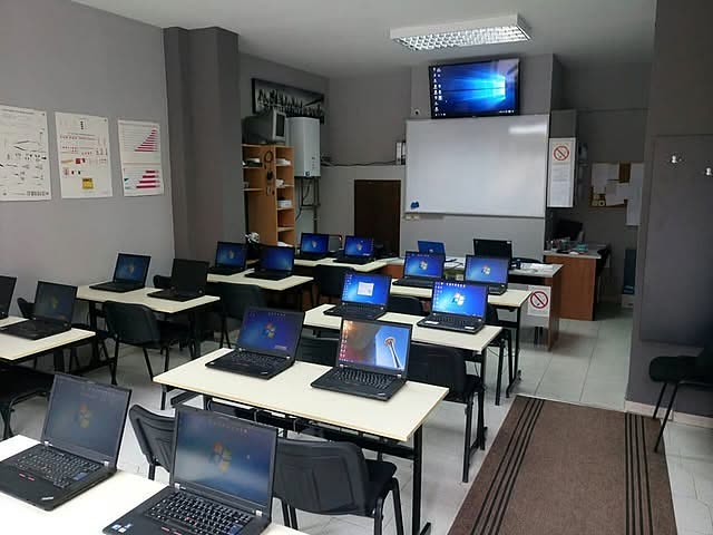 Učionica sa klupama i laptopovima, tablom i ekranom.